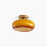Hailie mid-century modern ceiling lamp with warm amber glass disc and brass base in studio lighting