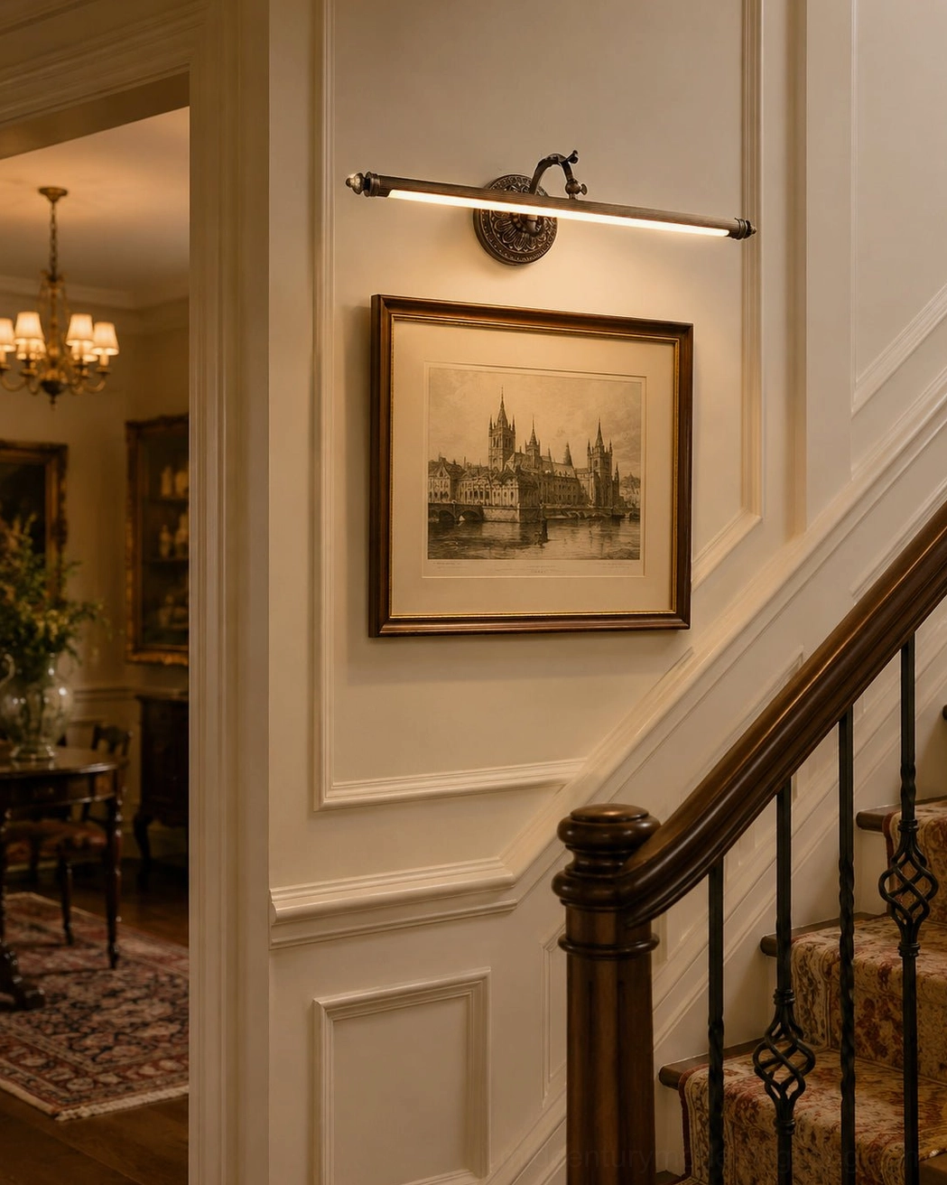 Dark patinated brass wall light mounted on wainscot wall flanking framed artwork in hallway