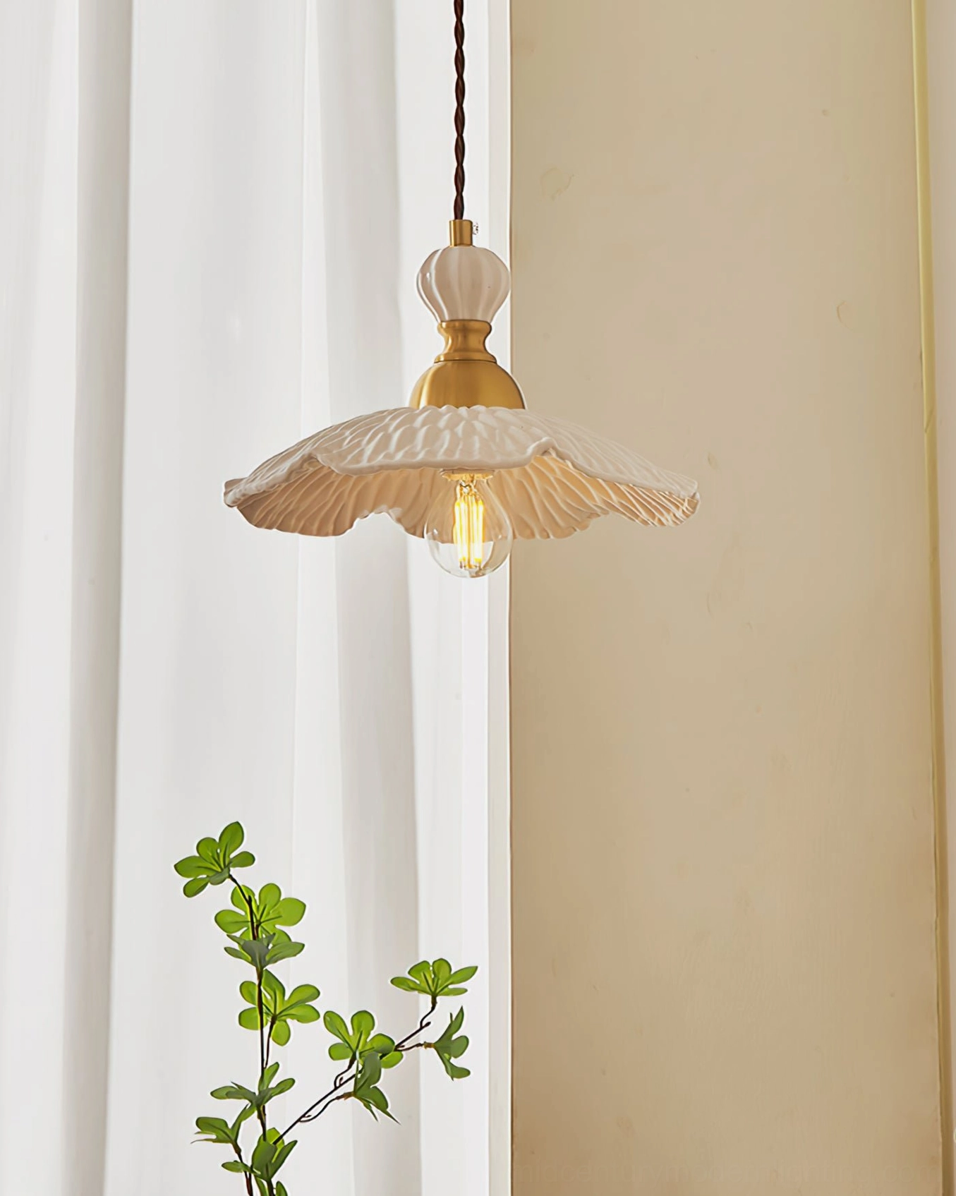 Handmade ceramic hanging lamp with flared petal silhouette glowing warm light near sheer curtain