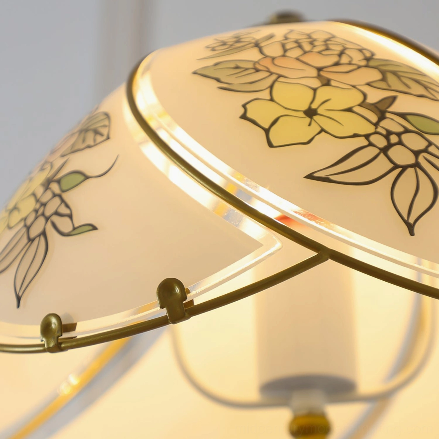 Extreme close-up studio shot of hand-painted yellow lily details on frosted stained glass with polished brass trim and internal bulb glow