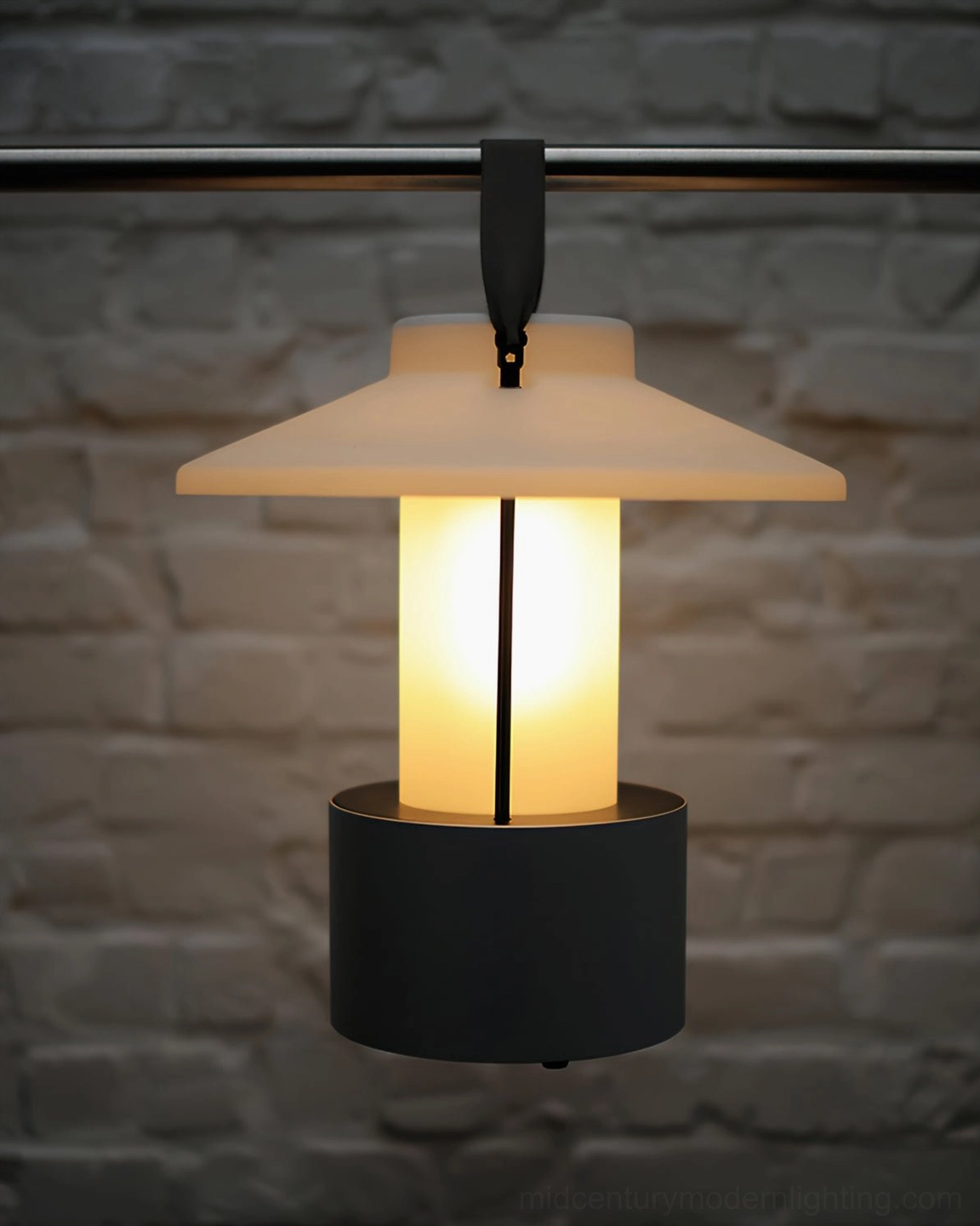 Portable outdoor lantern with black base and hanging strap mounted on brick wall
