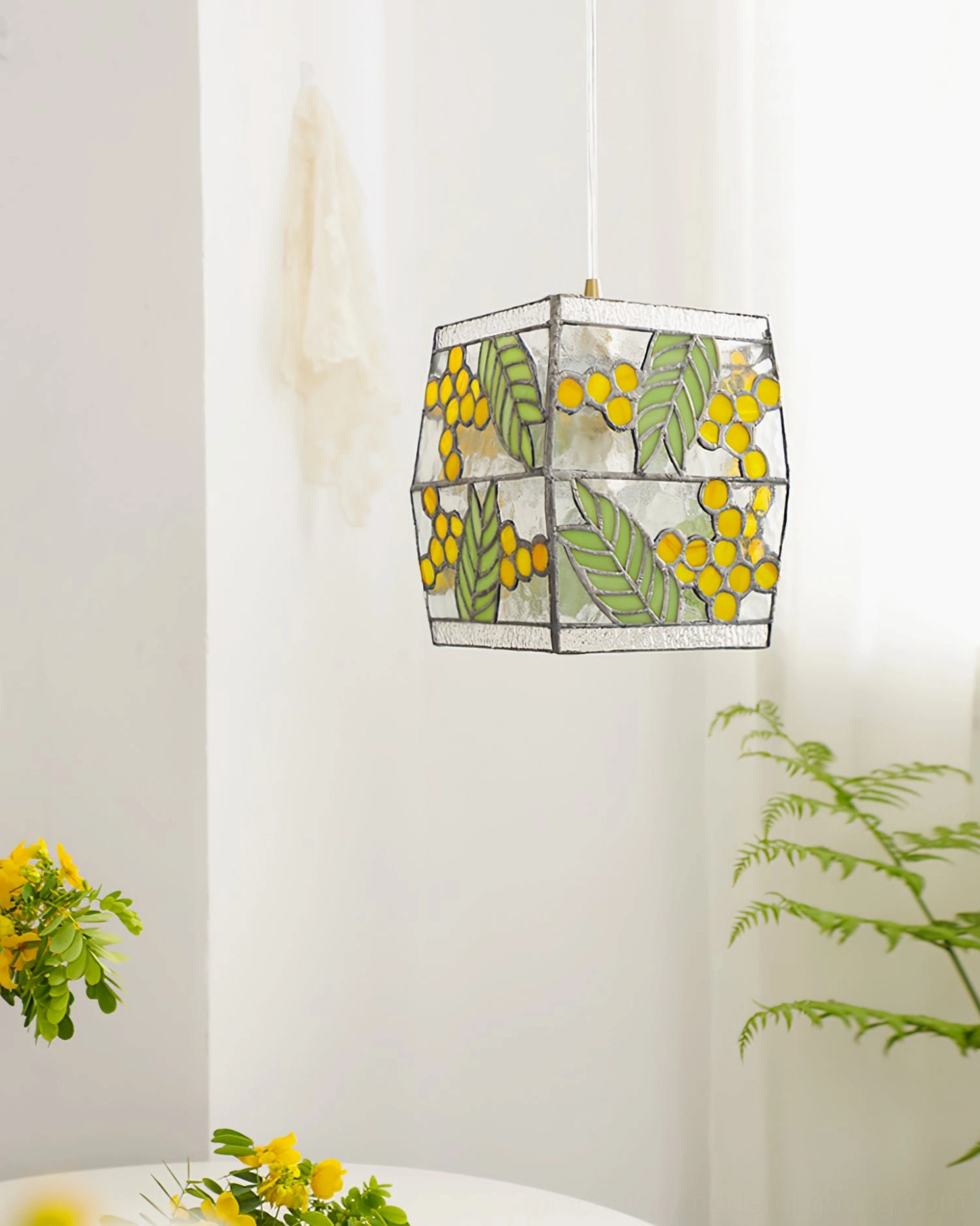 Hanging stained glass seed pendant lamp in bright minimalist room with green leaves and yellow glass pattern visible