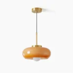 Harvey mid-century modern pendant light with warm amber glass shade and brass metal fixture, front view studio photography
