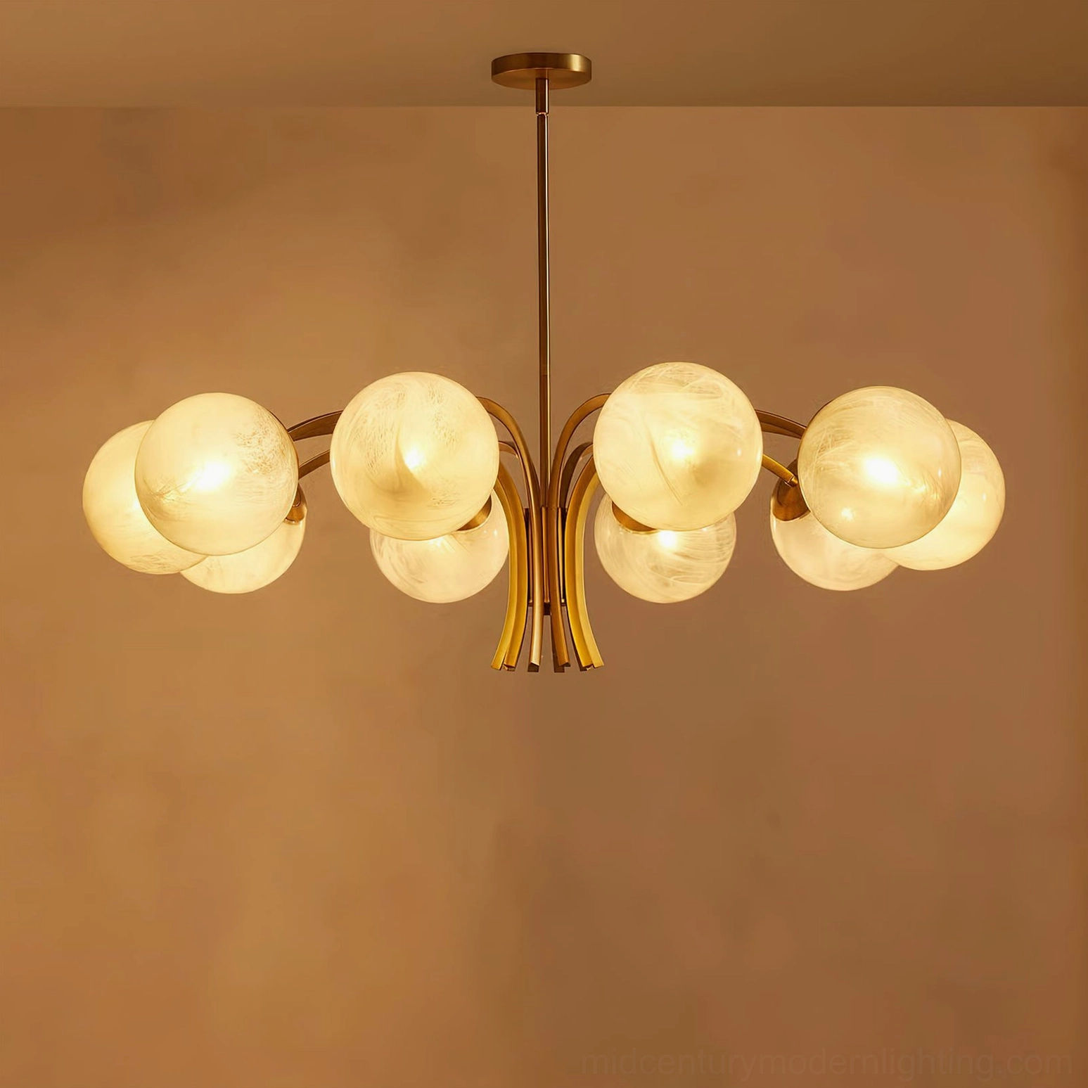 Illuminated brass globe chandelier with warm yellow LED light, overhead angled view against terracotta wall