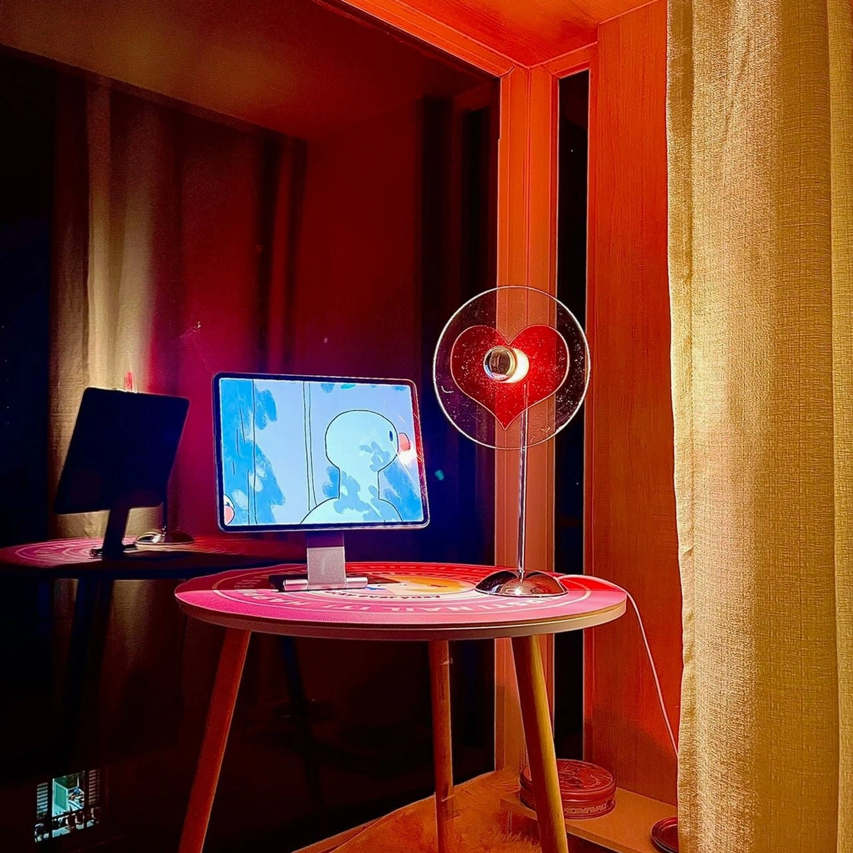 Heart-shaped projection lamp on pink round side table in modern home office, casting red heart ambient glow