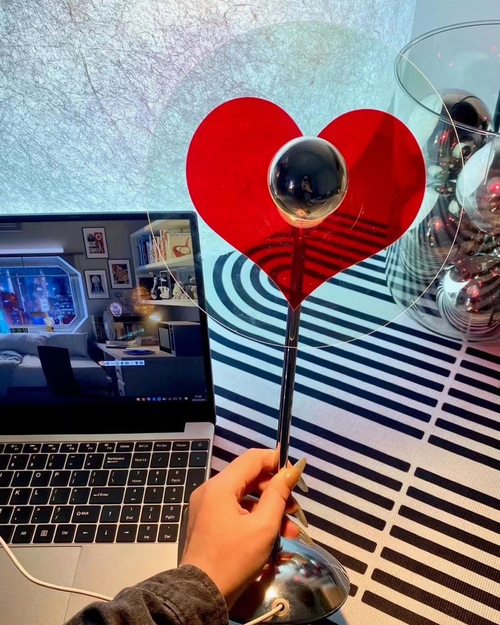 Heart-shaped table lamp on workspace desk with striped mat and laptop, modern home office décor