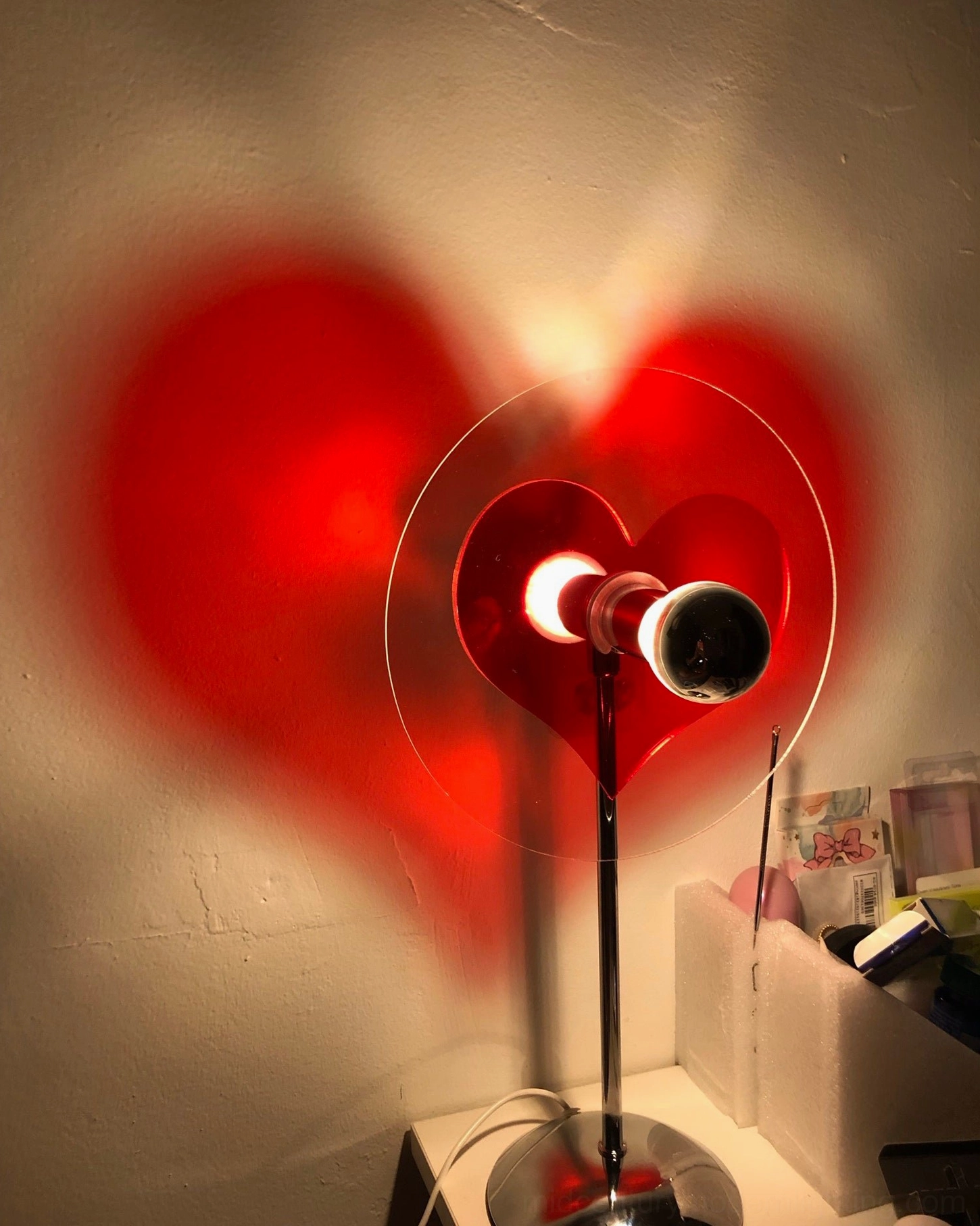 Low angle close-up of heart projection lamp casting glowing red heart shadow on indoor wall surface