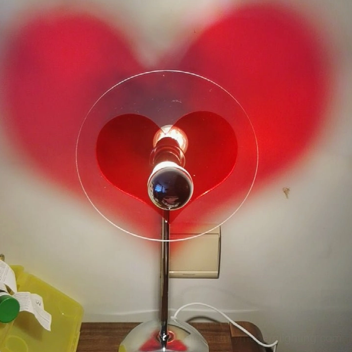 Heart projection lamp in bedroom nightstand setting, creating warm intimate lighting ambiance