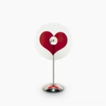Heart-shaped red LED projection table lamp on white background, minimalist modern design with chrome metal frame and clear acrylic base