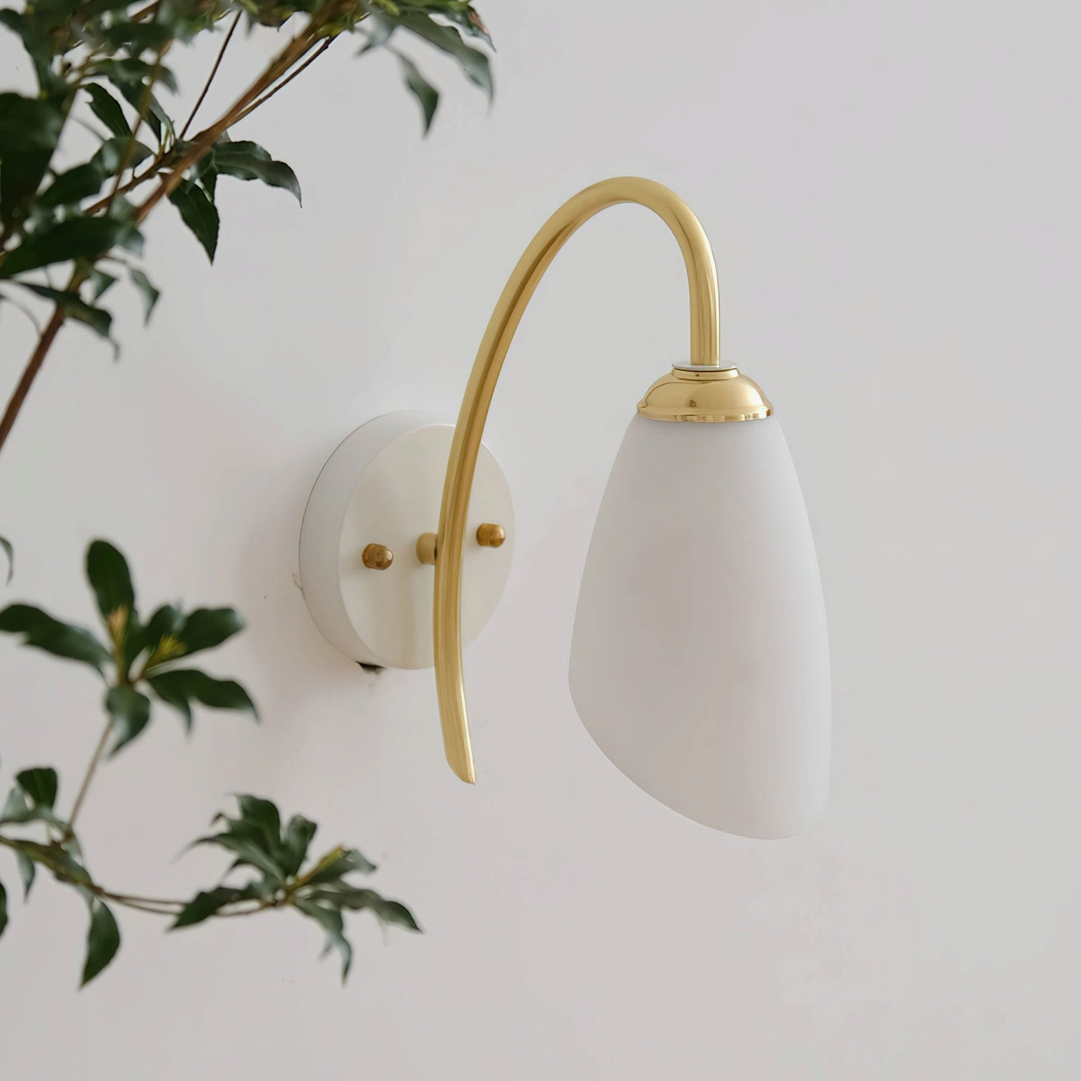 Hector wall lamp side profile showing curved brass arm and diffused light with indoor greenery