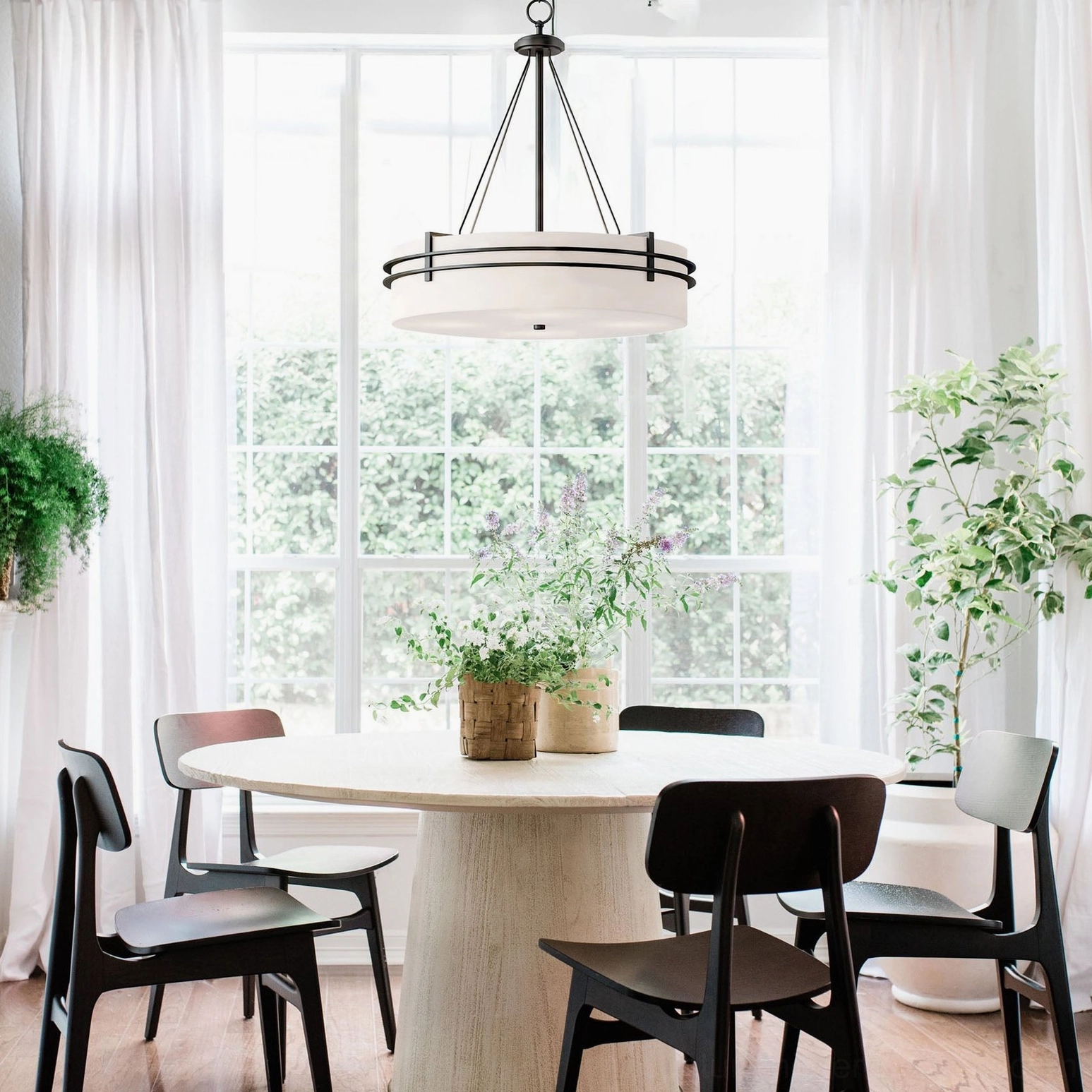 Modern Heddle drum chandelier with metal hardware displayed above round dining table in sunlit casual space