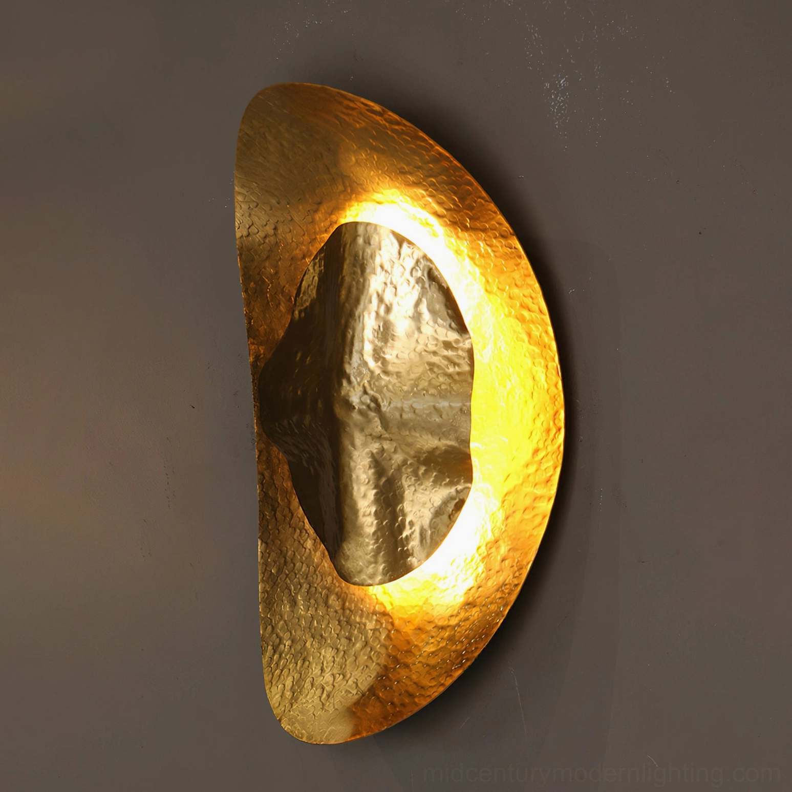 Side profile of Helios hammered brass sconce on dark gray accent wall with backlit rim detail and half-oval metalwork
