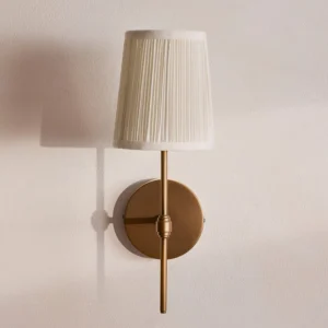 Henley wall sconce mounted on warm-toned interior wall with brass base and tapered pleated shade