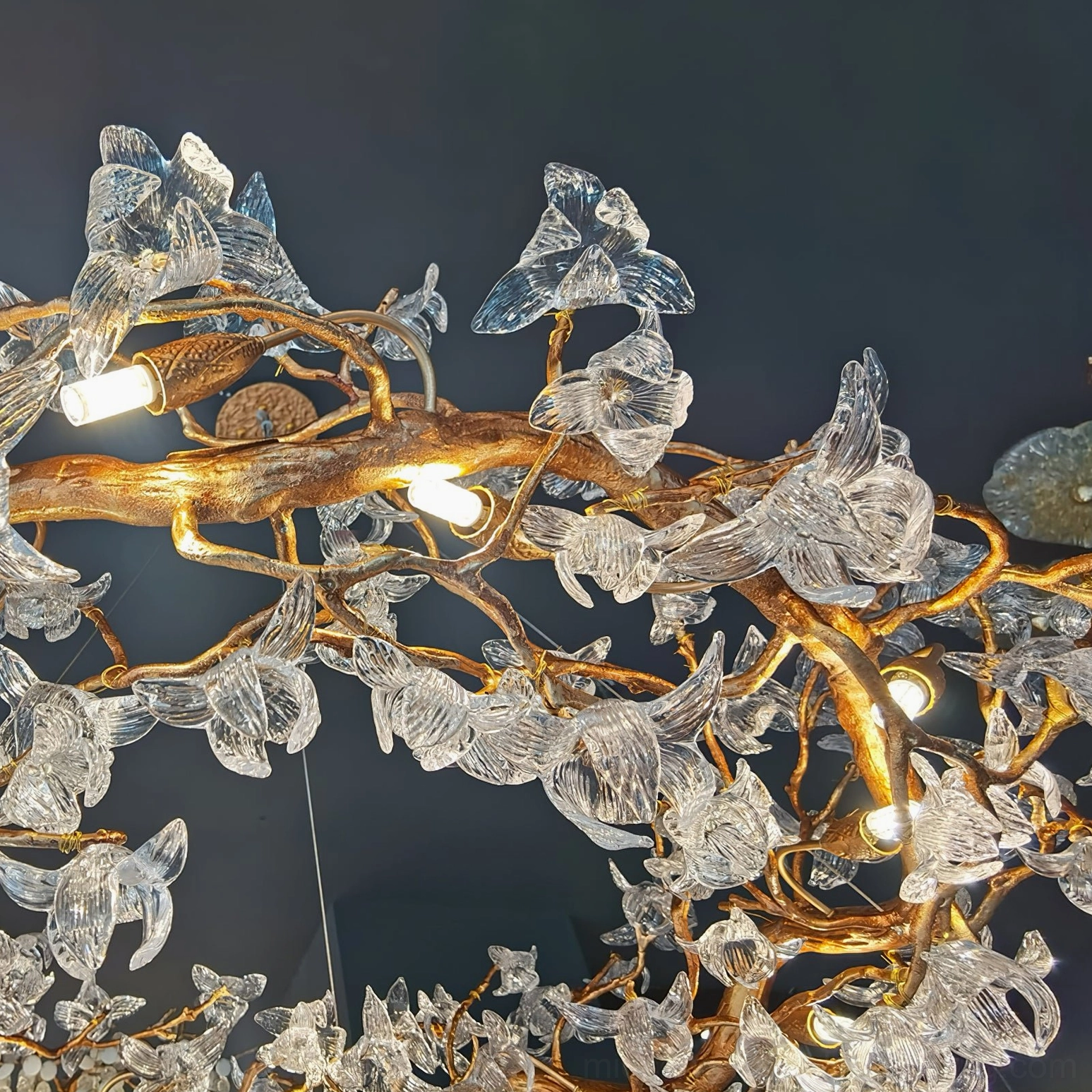 Macro detail of hibiscus chandelier showing gilded brass branches and clear crystal flower petals with LED bulbs