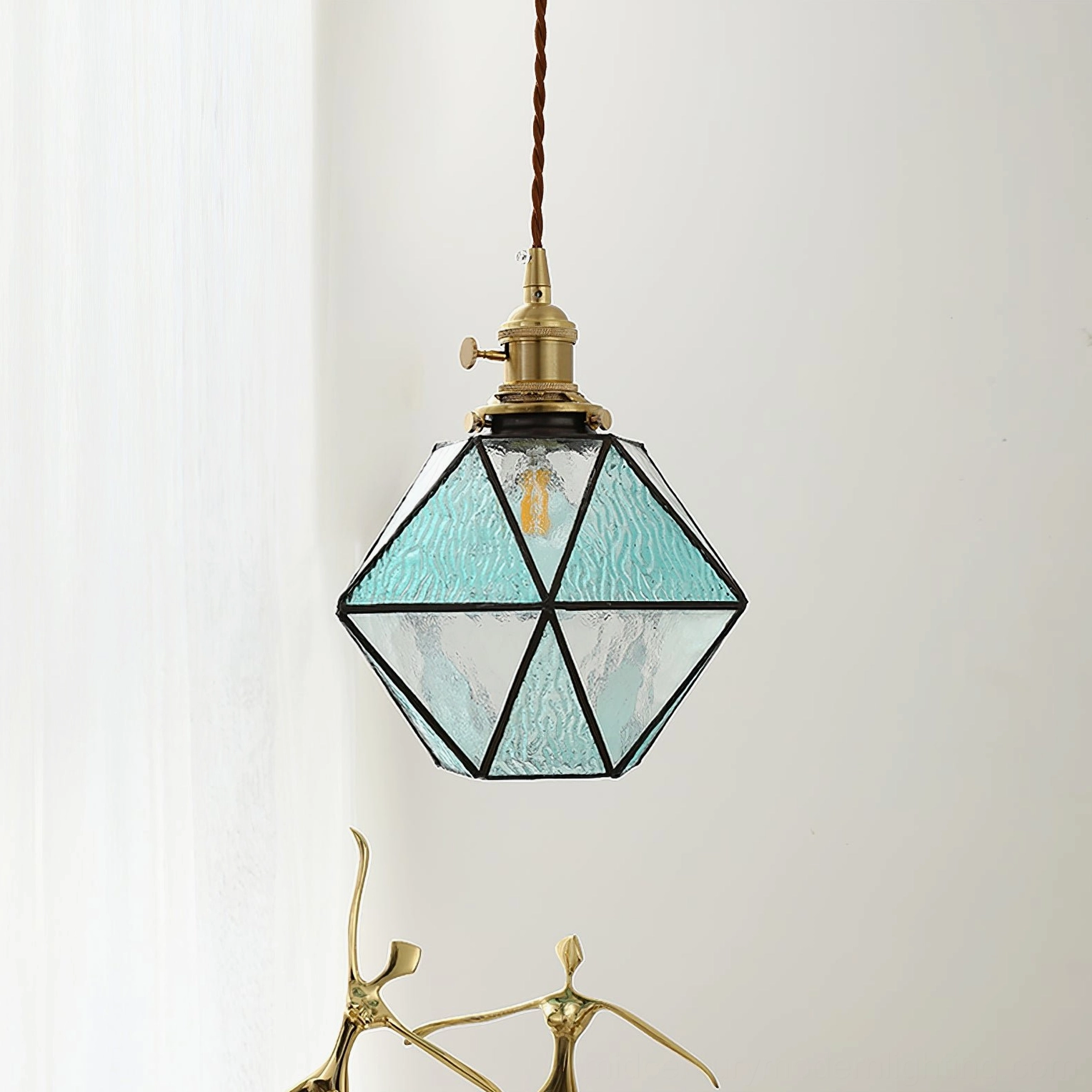 Hiro blue geometric pendant lamp with textured glass panels and golden brass trim, side frontal view in bright room with sheer curtains