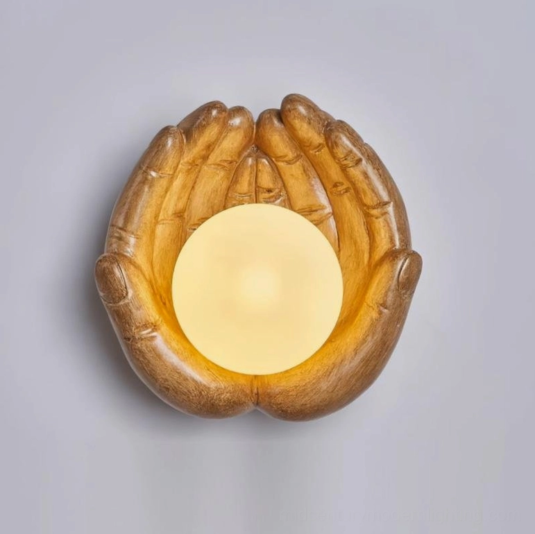 Front-facing holding hands wall sconce in warm wood tone, featuring realistic hand details and luminous glass sphere on neutral gray background