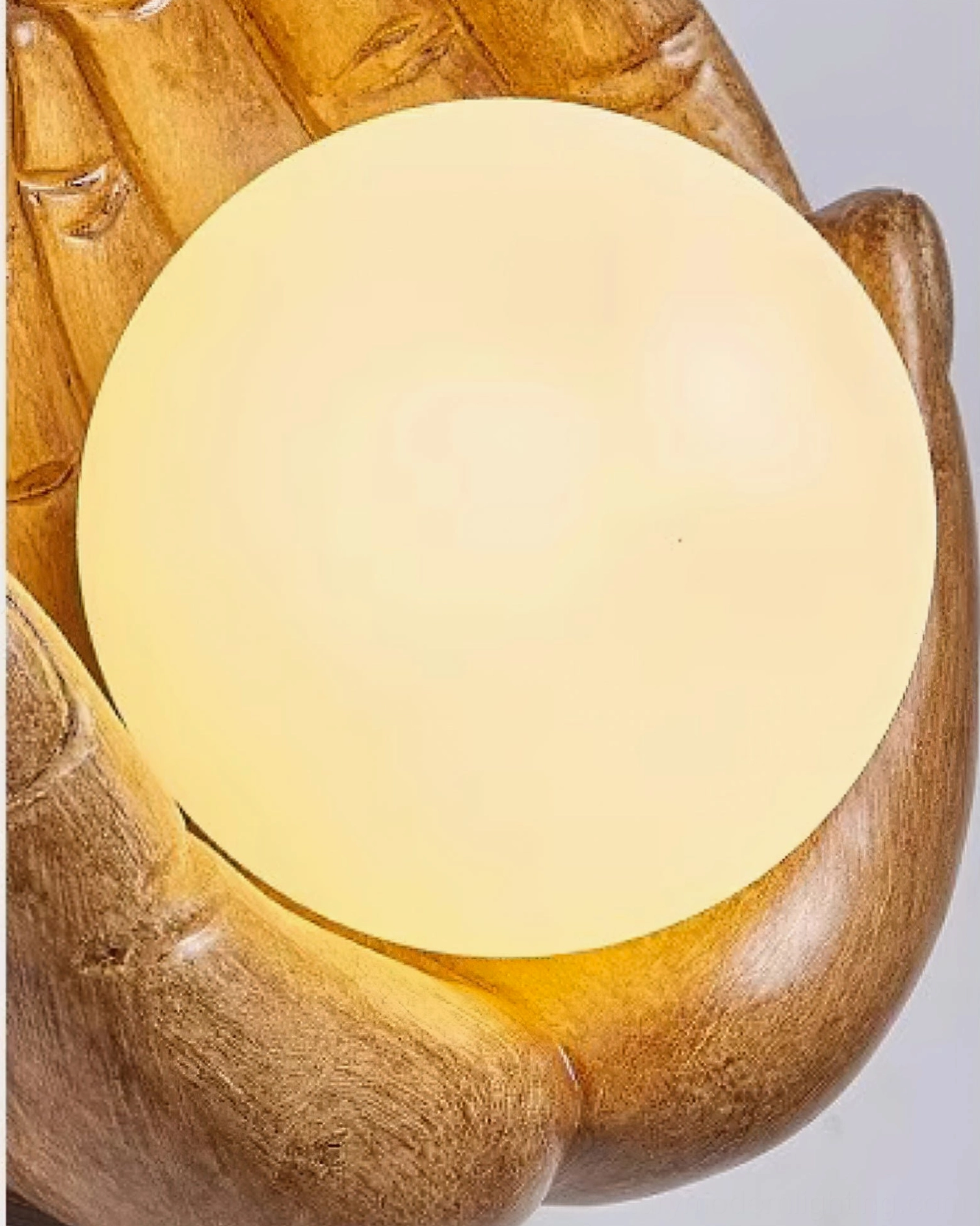 Detailed front close-up of holding hands wall lamp highlighting oversized warm glass orb nestled in carefully sculpted wooden hands