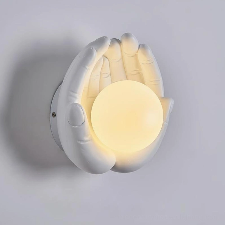 Holding hands wall sconce in clean white matte resin with warm yellow glass orb, side close-up showcasing craftsmanship and light diffusion