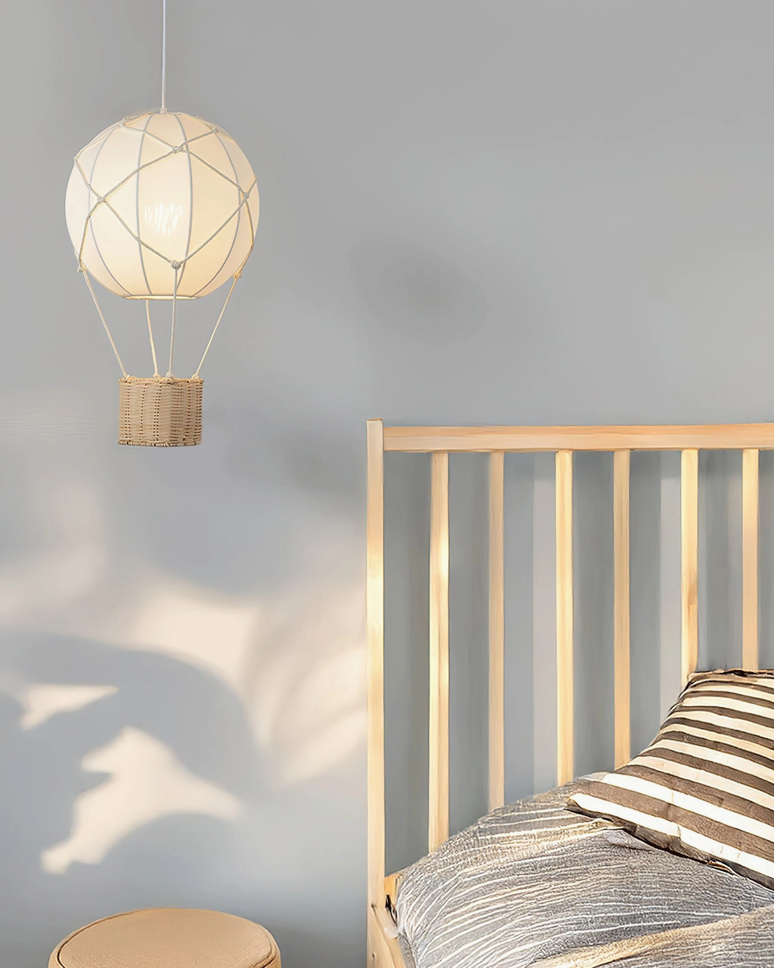 Hot air balloon pendant light hanging over wooden bed in cozy bedroom with soft natural wall shadow