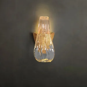 Icarus droplet glass wall lamp illuminated with warm light against dark gray wall showing textured glass detail
