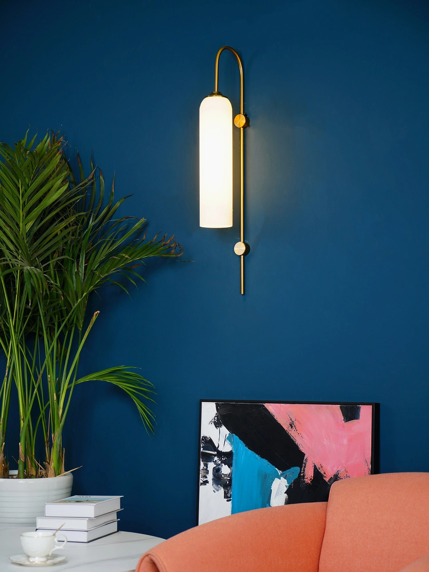 Illuminated glass wall sconce with curved brass arm and hanging spherical detail glowing against dark blue wall