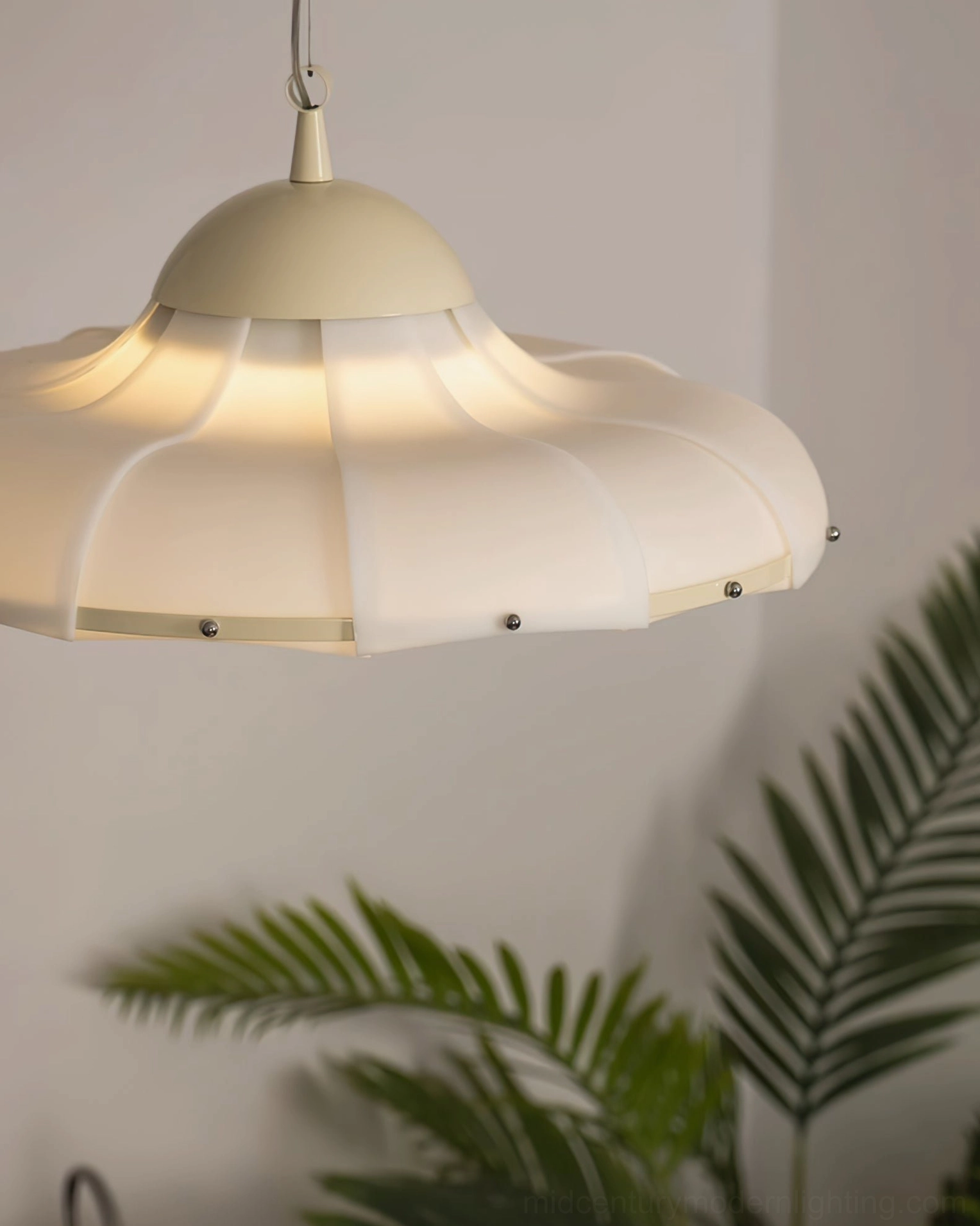 Illuminated swirl pendant lamp in warm cream finish with palm plants in cozy indoor setting