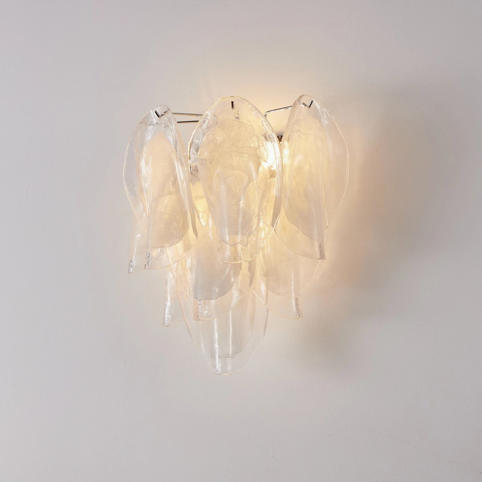 Ina modern wall sconce illuminated showing soft diffused light through curved glass petals