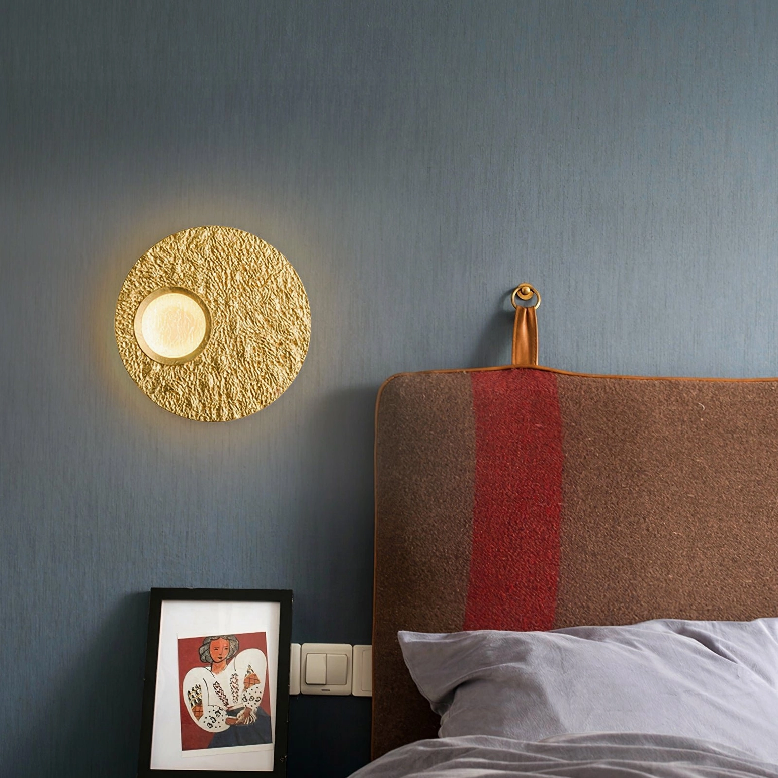 Gold Infinity LED wall lamp mounted in modern bedroom providing warm ambient lighting above striped headboard