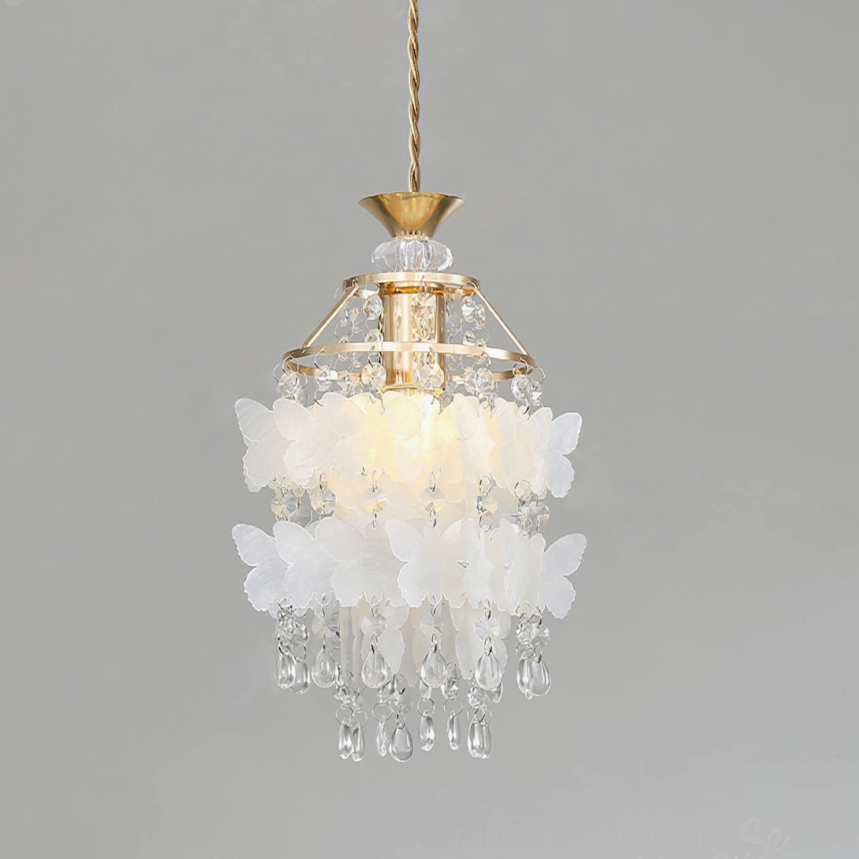 Close-up illuminated view of Jasinski butterfly pendant in gold finish showing layered white frosted butterfly decor with brass hardware and crystal droplets