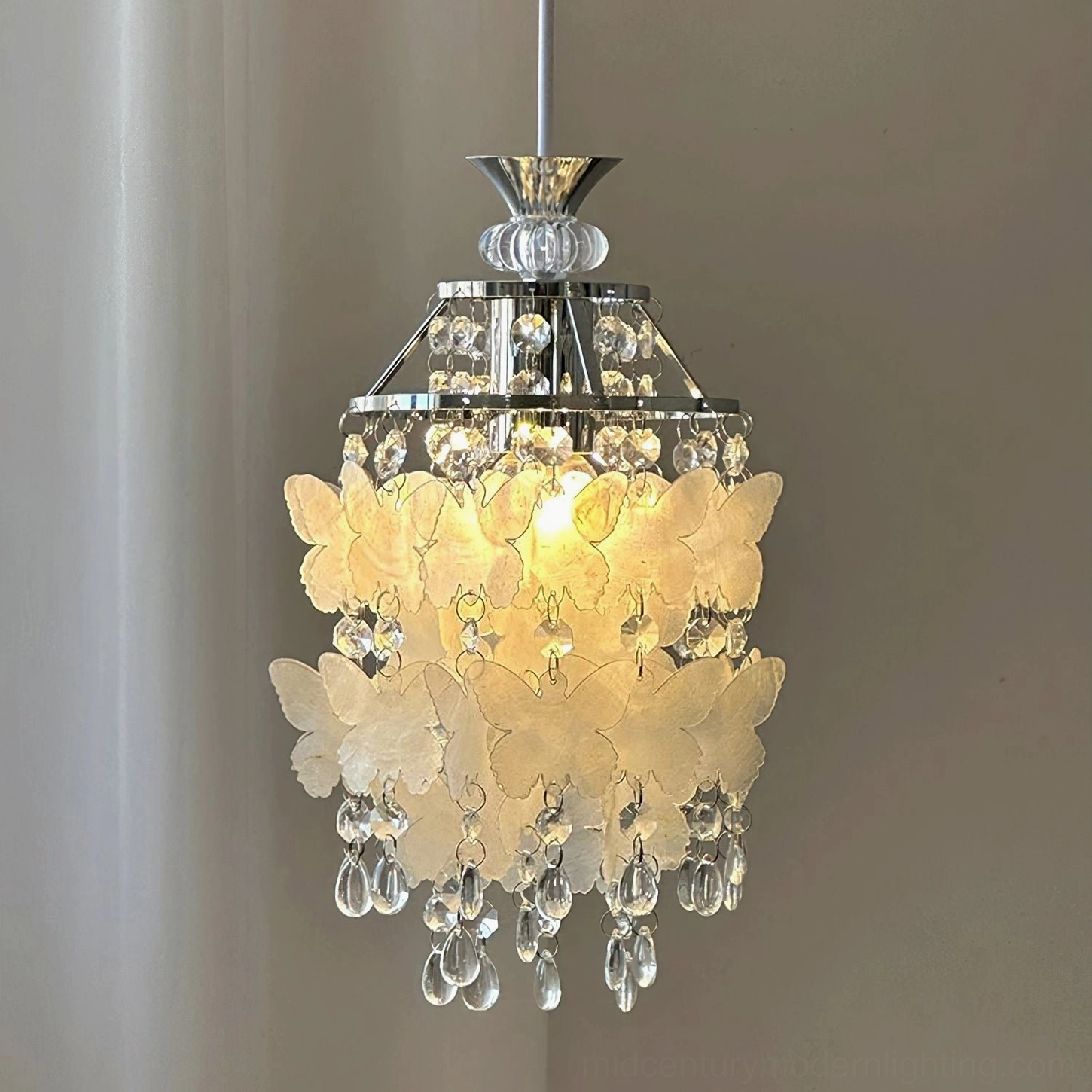 Illuminated Jasinski butterfly pendant light with warm glowing bulb, mixed silver and brass hardware creating ambient light in home interior