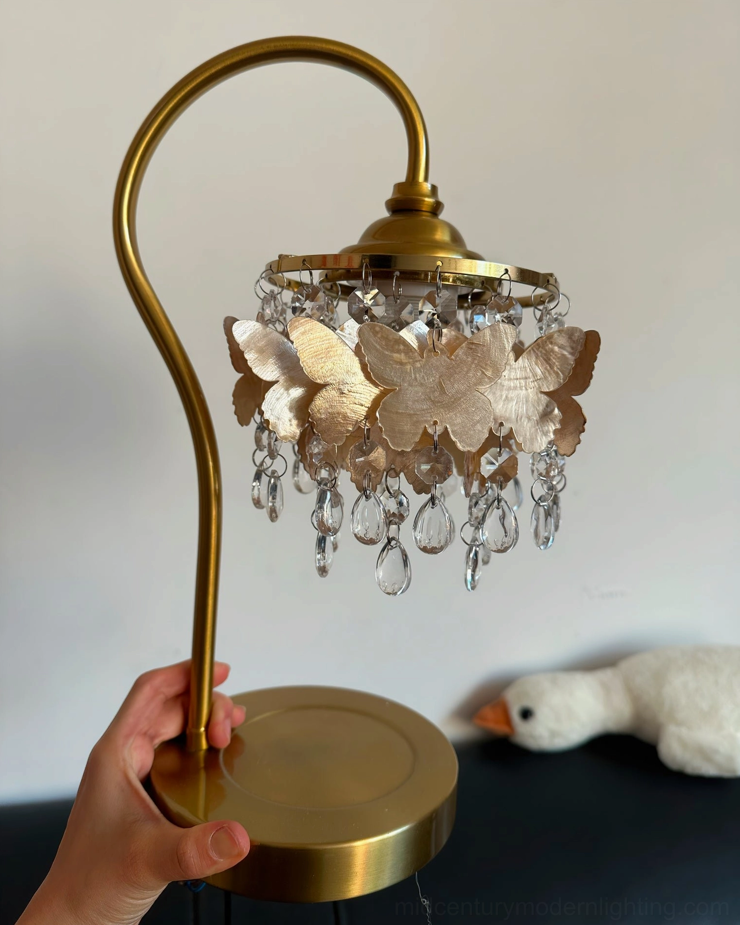 Close-up of hand holding polished brass base of Jasinski butterfly table lamp with crystal accents visible