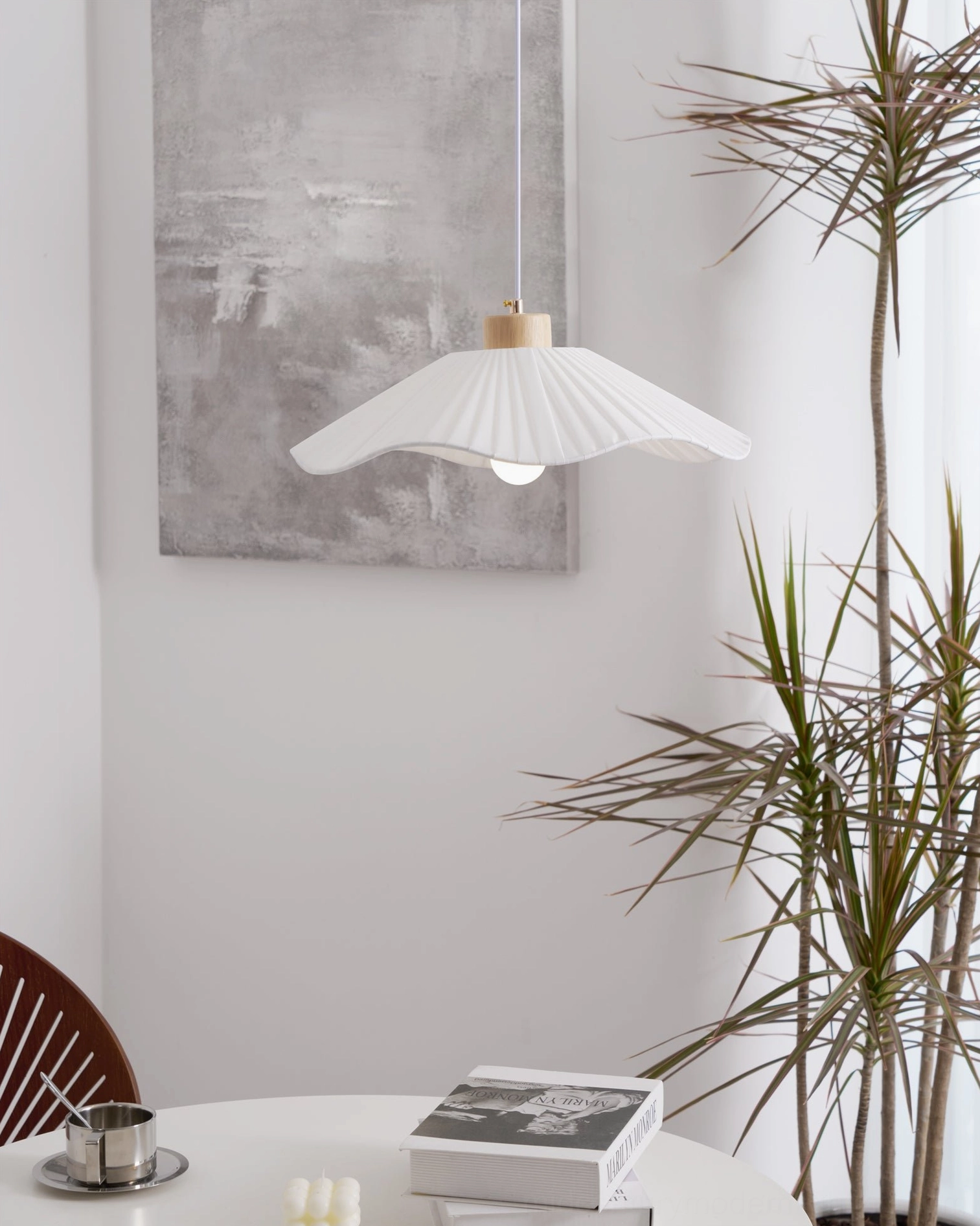 Jimi pendant light positioned above dining area with green potted plants, soft white pleated shade creating ambient lighting