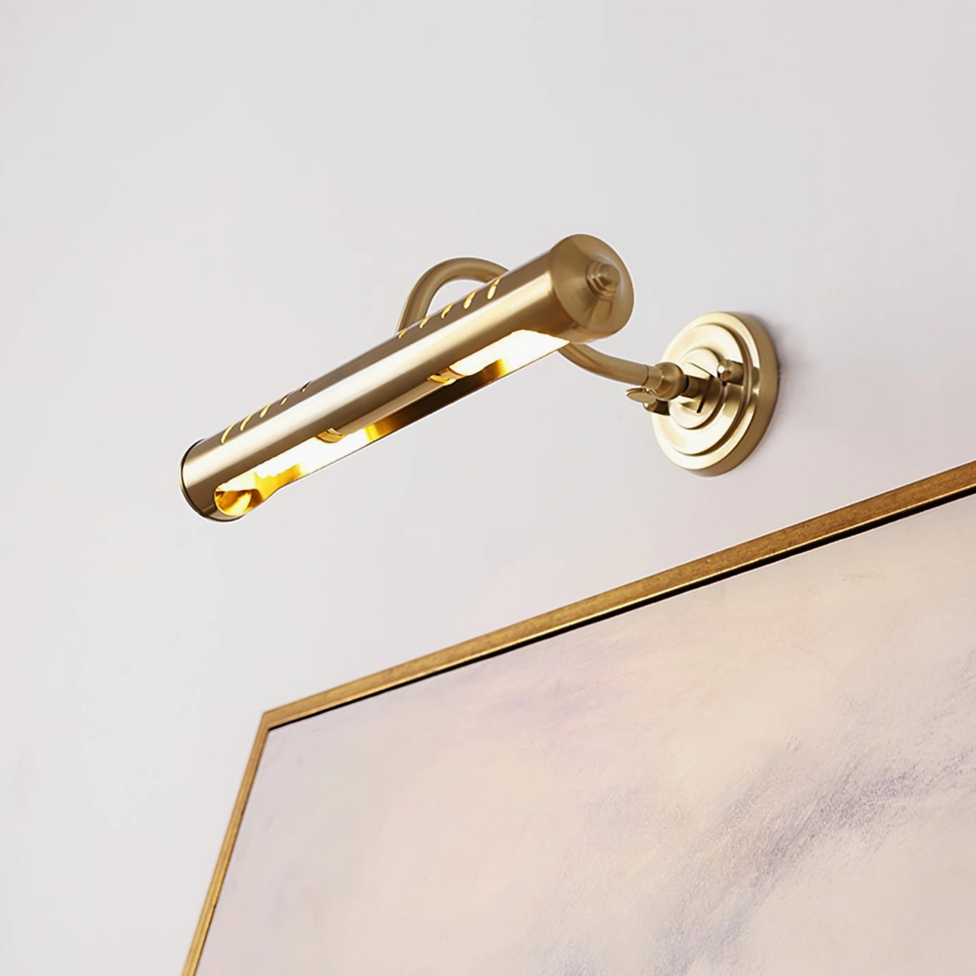 Joely adjustable brass wall light with rotatable fixture head positioned near framed artwork