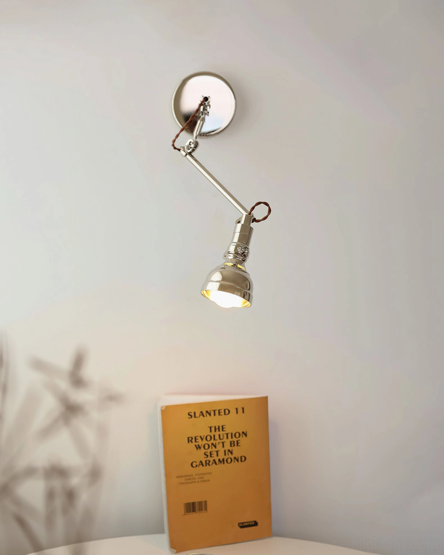 Low-angle frontal view of articulated swing arm wall sconce in dining corner, silver metal construction