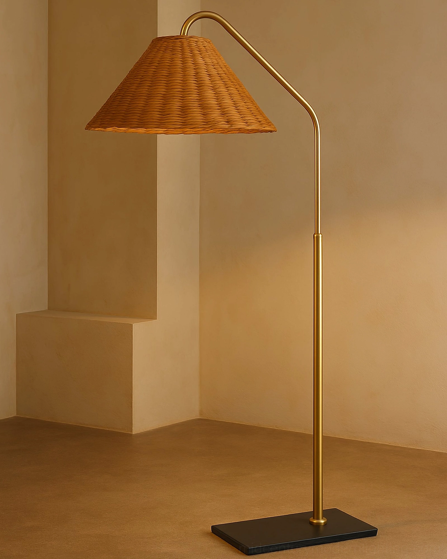 Juno rattan arc floor lamp with polished brass finish and black square base, minimalist indoor corner display