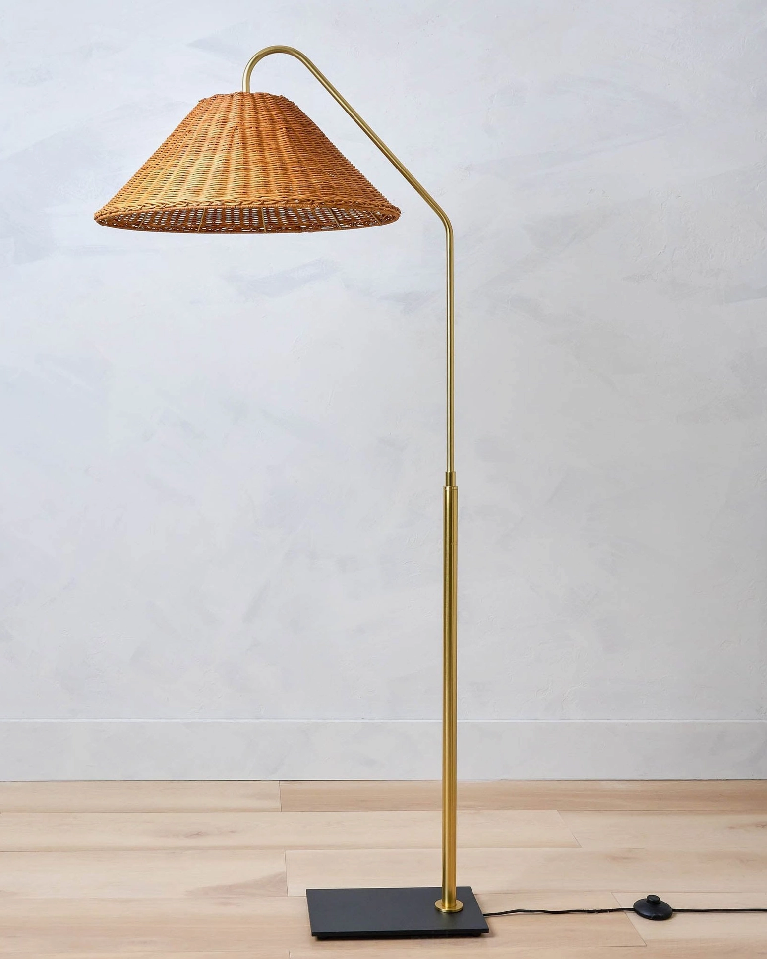 Juno arc rattan floor lamp with visible power cable on clean wood-floored surface, direct front view showcase