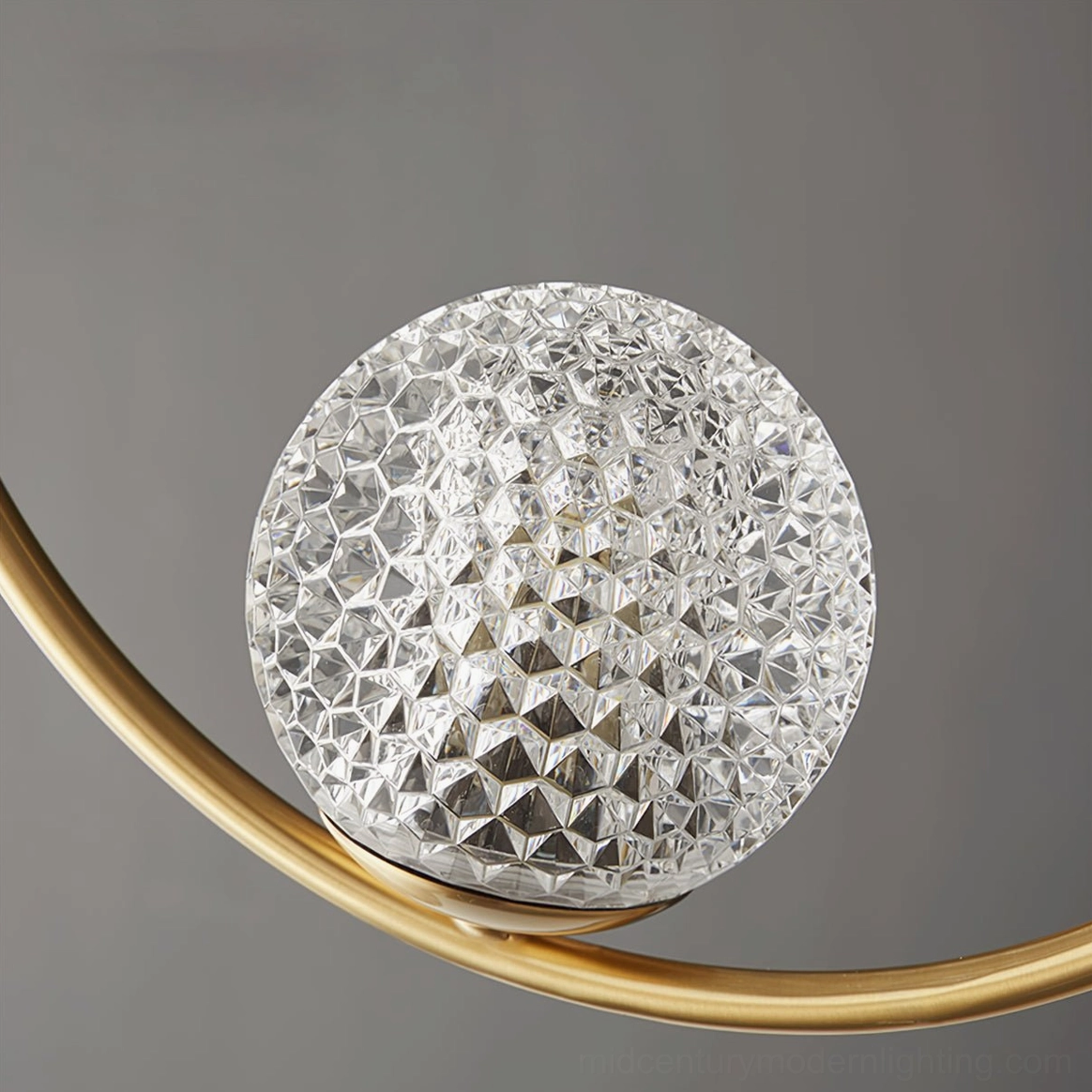 Unlit Jupiter pendant lamp showing textured faceted clear glass shade geometry with gold brass mounting arm, studio macro front view