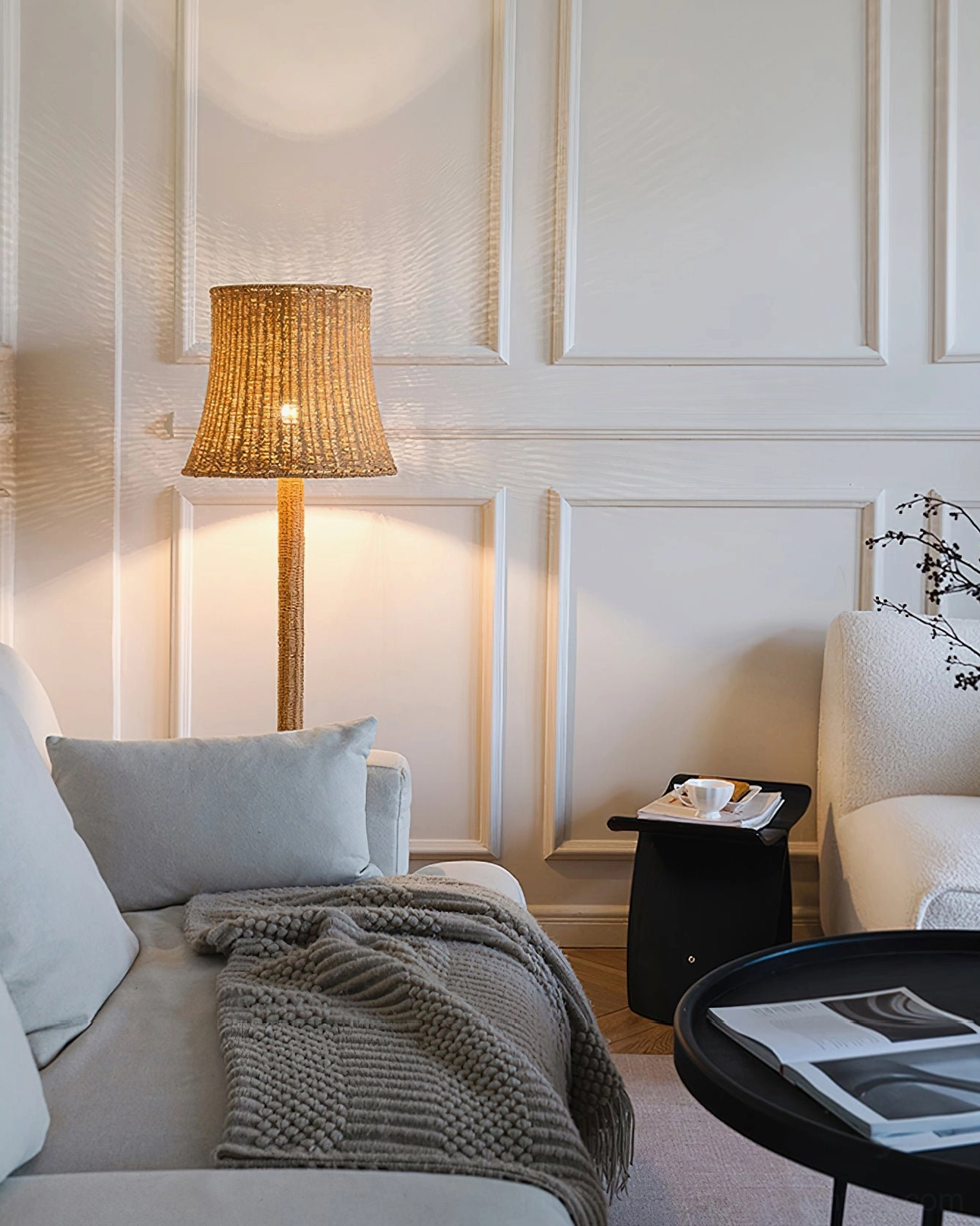 Kakasi handwoven rattan floor lamp in living room with wooden armchair and stacked books, cozy reading corner