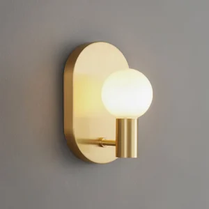Kalux brass wall lamp with warm gold finish and glowing frosted glass bulb close-up side angle