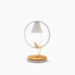 Kamilah modern table lamp with circular white metal frame and bird ornament on natural wood base, front view studio photography