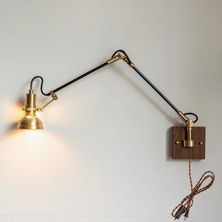 Kane plug-in wall lamp with illuminated bulb showing brass swing arm joints in articulated position, three-quarter view highlighting sculptural design
