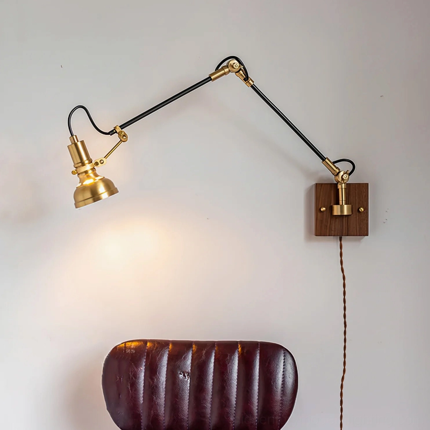 Kane swing arm wall lamp positioned beside leather chair with visible power cord, showing adjustable positioning for reading light application