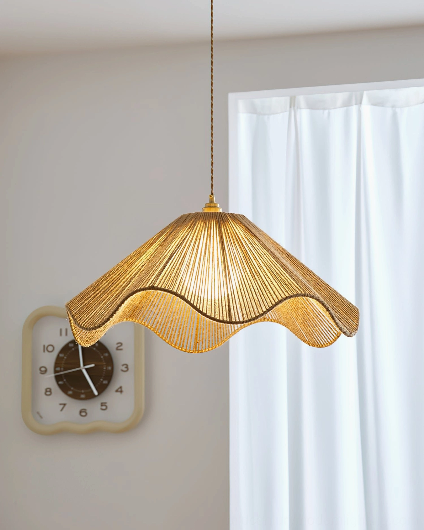 Karai coastal pendant light low front view illuminated above indoor wall space with sheer curtain and wall clock in boho setting