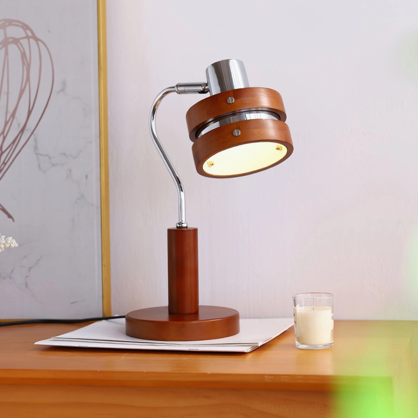 Karry table lamp glowing with warm yellow light against marble wall art backdrop, frontal view