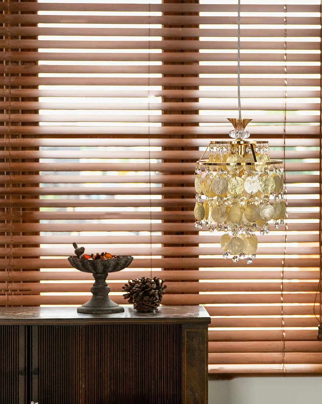 Small Katinka shell pendant light in dining nook with transparent and beige capiz shells, gold metal hardware, side distant view with wooden blinds