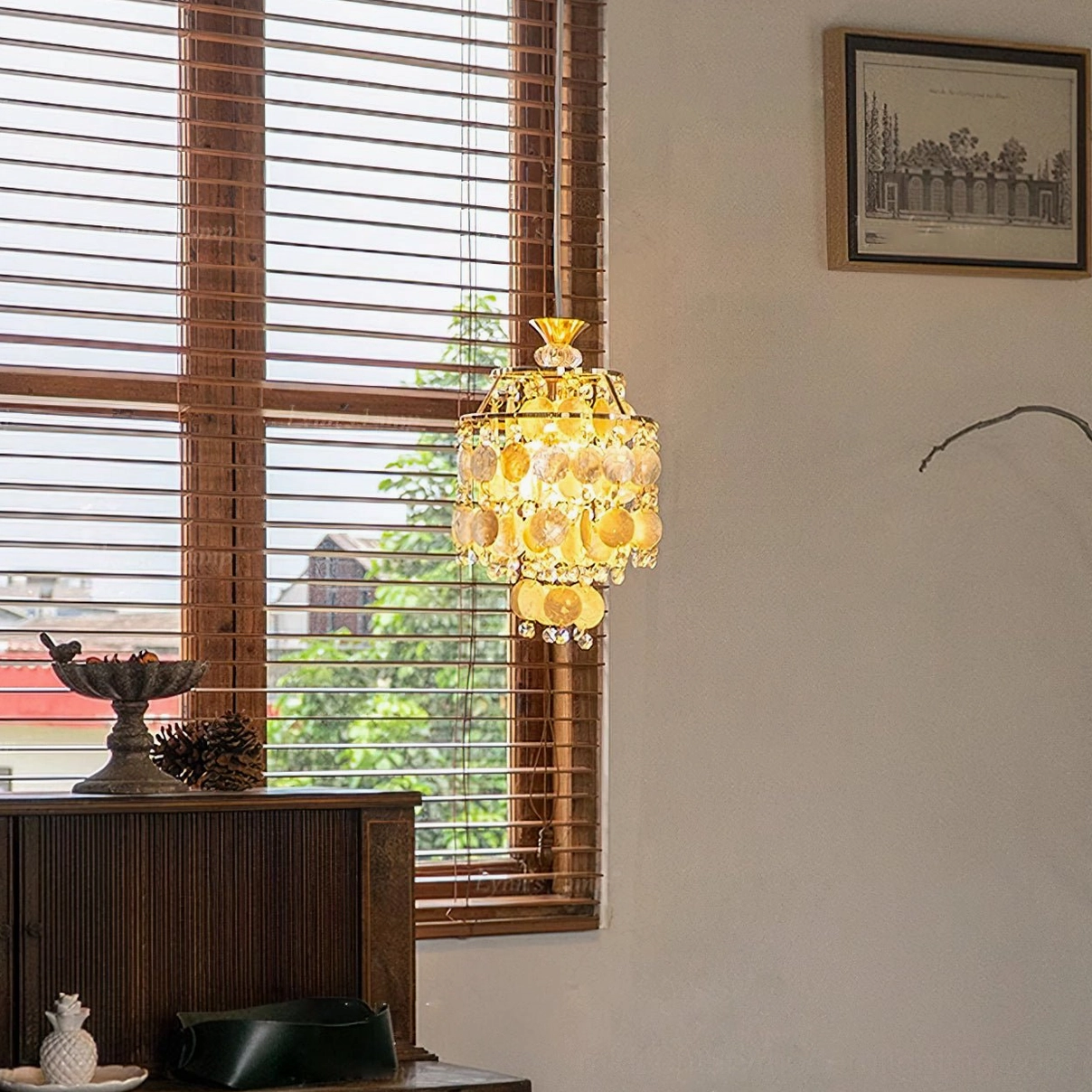 Lit Katinka capiz shell pendant in vintage home corner, warm amber-gold shells with dangling crystals, side distant view