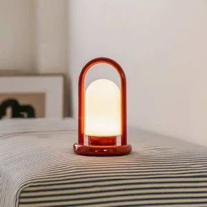 Kero portable lamp lit on bedroom nightstand, casting warm glow over striped bedding