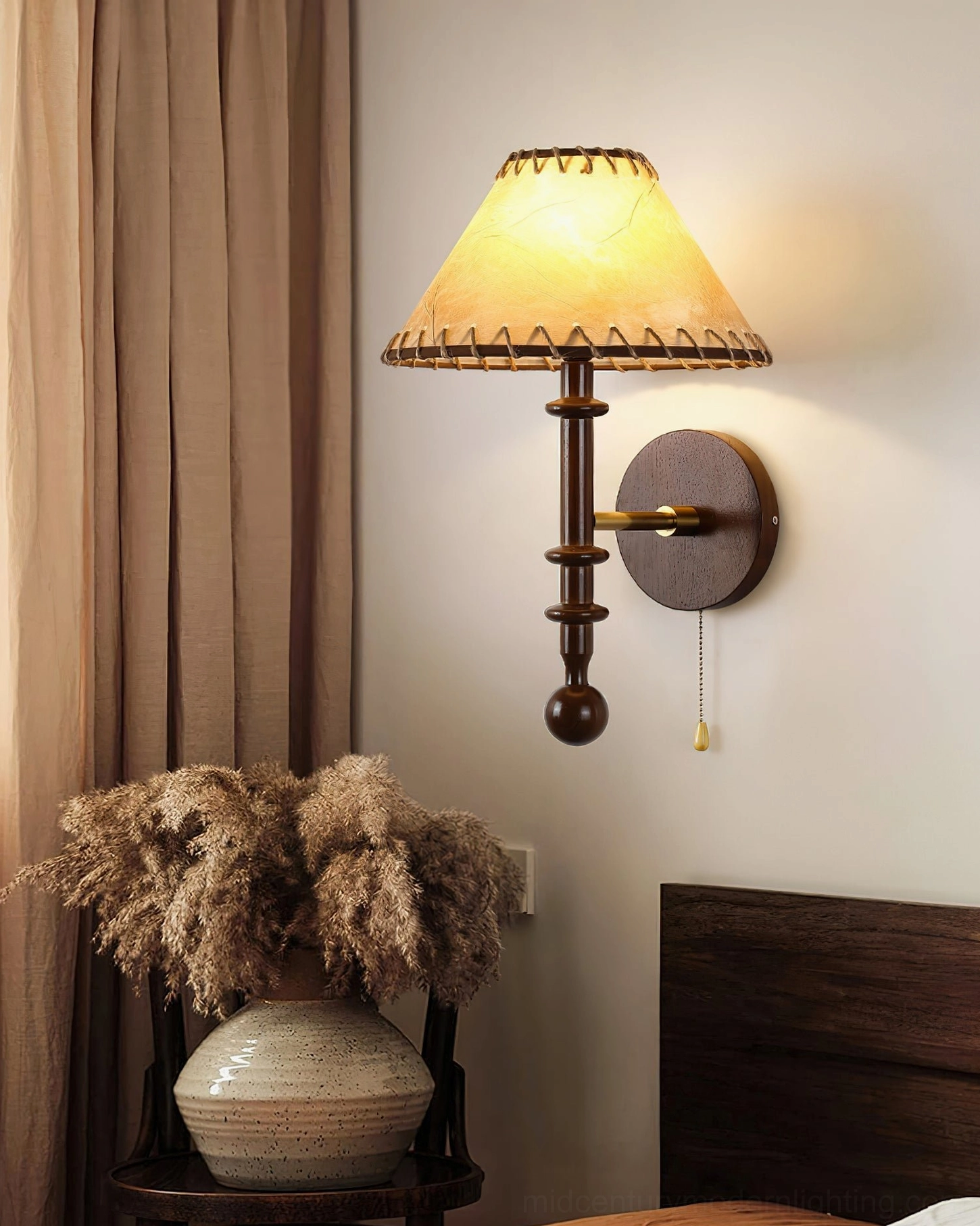 Warm glowing Kibo wall lamp positioned in bedroom bedside nook with pampas grass and wooden headboard styling