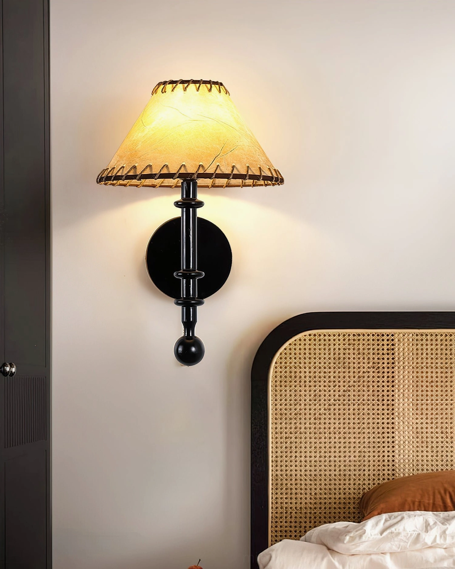 Minimalist Kibo wood sconce with all-black metal hardware glowing warm light near rattan headboard