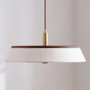 Kimber pendant lamp three-quarter view showing white fabric shade, brown wood edge, and polished brass hardware in minimalist interior